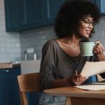 Woman drinking Coffee while looking into her PC and holding a sheet of paper sustainable business for women