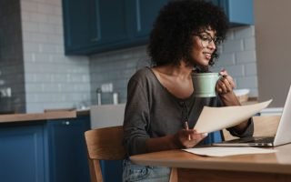 Woman drinking Coffee while looking into her PC and holding a sheet of paper sustainable business for women
