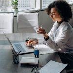 A woman sitting on a large desk, a laptop and papers on the desk, she is holding a glass -how to attract aligned clients tips